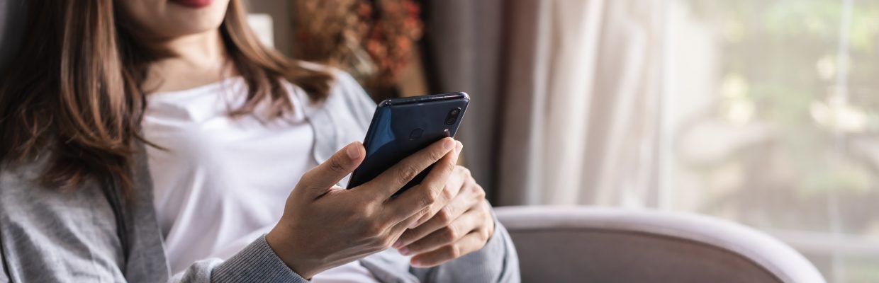 Young Woman Lying On Sofa At Living Room And Using Cell Phone At Home
